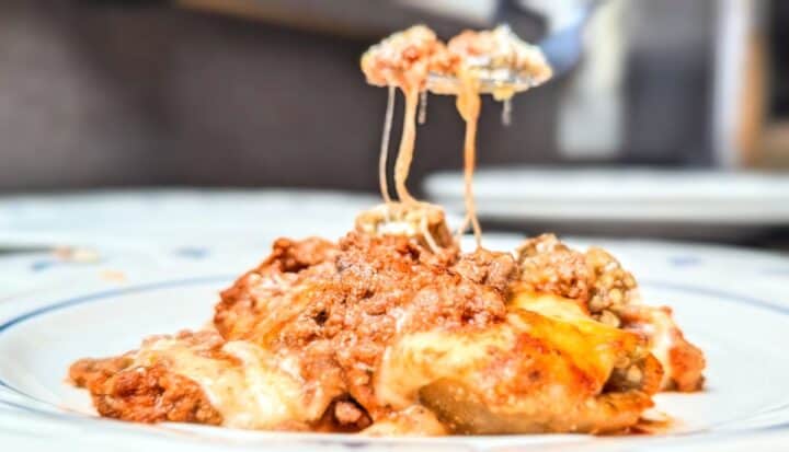 Lifting a serving of cheesy eggplant casserole with a long, melted cheese pull.