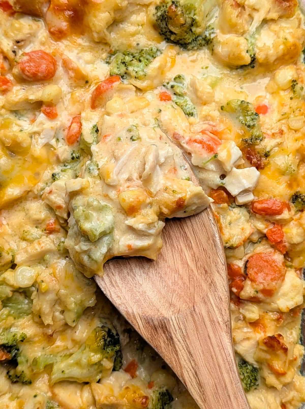 spoon lifting cheesy casserole with broccoli and carrots and chicken