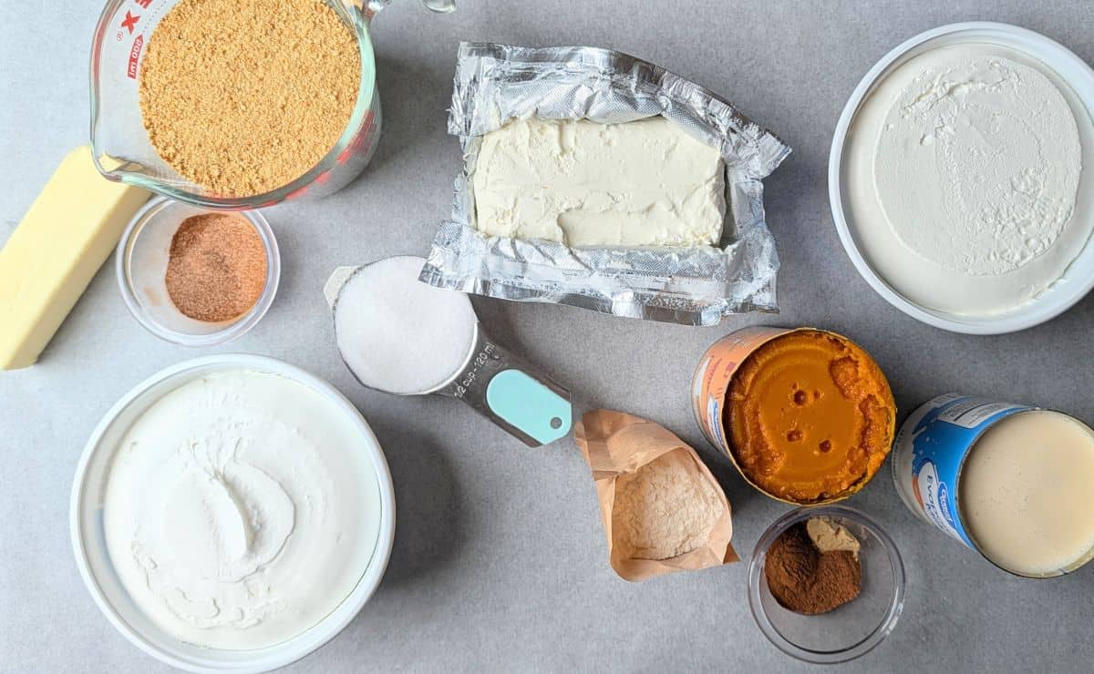 Overhead view of ingredients for a pumpkin lush recipe, including graham crackers, pumpkin puree, cream cheese, and whipped topping.