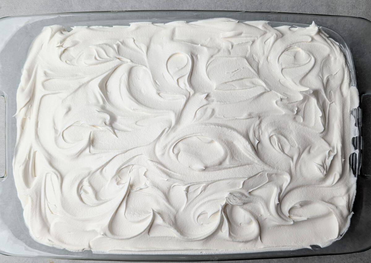 The final layer of a pumpkin lush recipe, showing fluffy whipped topping spread smoothly over the pumpkin layer.
