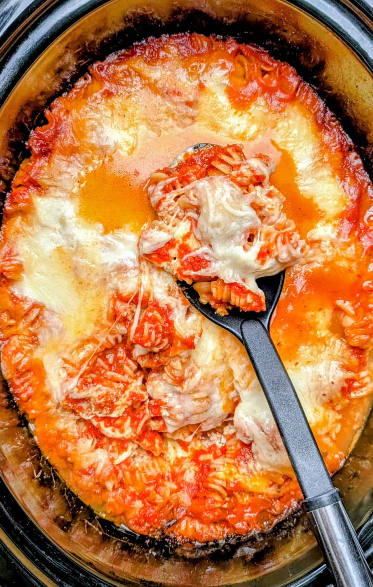 top down view of ladle scooping noodles cheese and sauce from slow cooker after ziti is finished