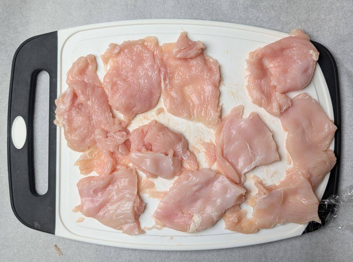 Raw chicken cutlets pounded thin on a white cutting board, the first step to making healthy chicken parmesan.