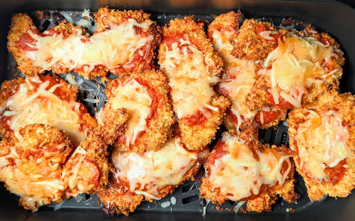 Breaded chicken cutlets for healthy chicken parmesan cooking inside an air fryer basket.