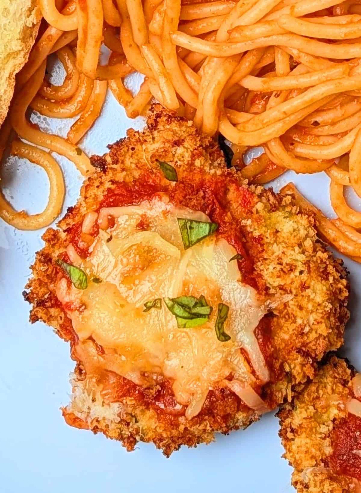 chicken parmesan cutlet on plate topped with mozzarella and basil
