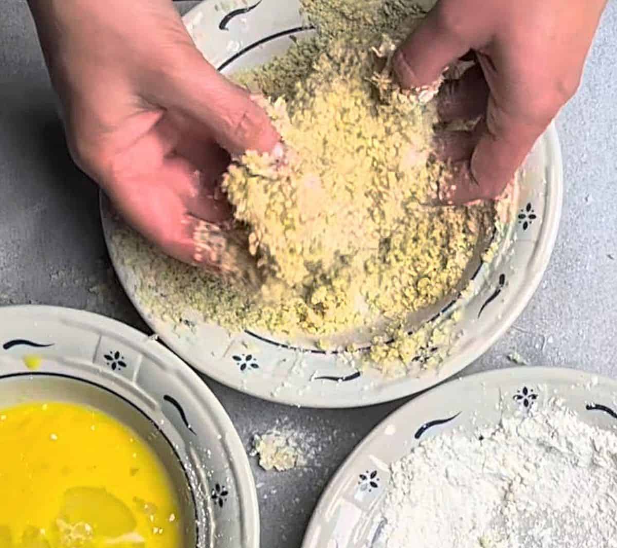 A chicken cutlet being coated in a bowl of panko breadcrumbs and seasonings to make healthy chicken parmesan.