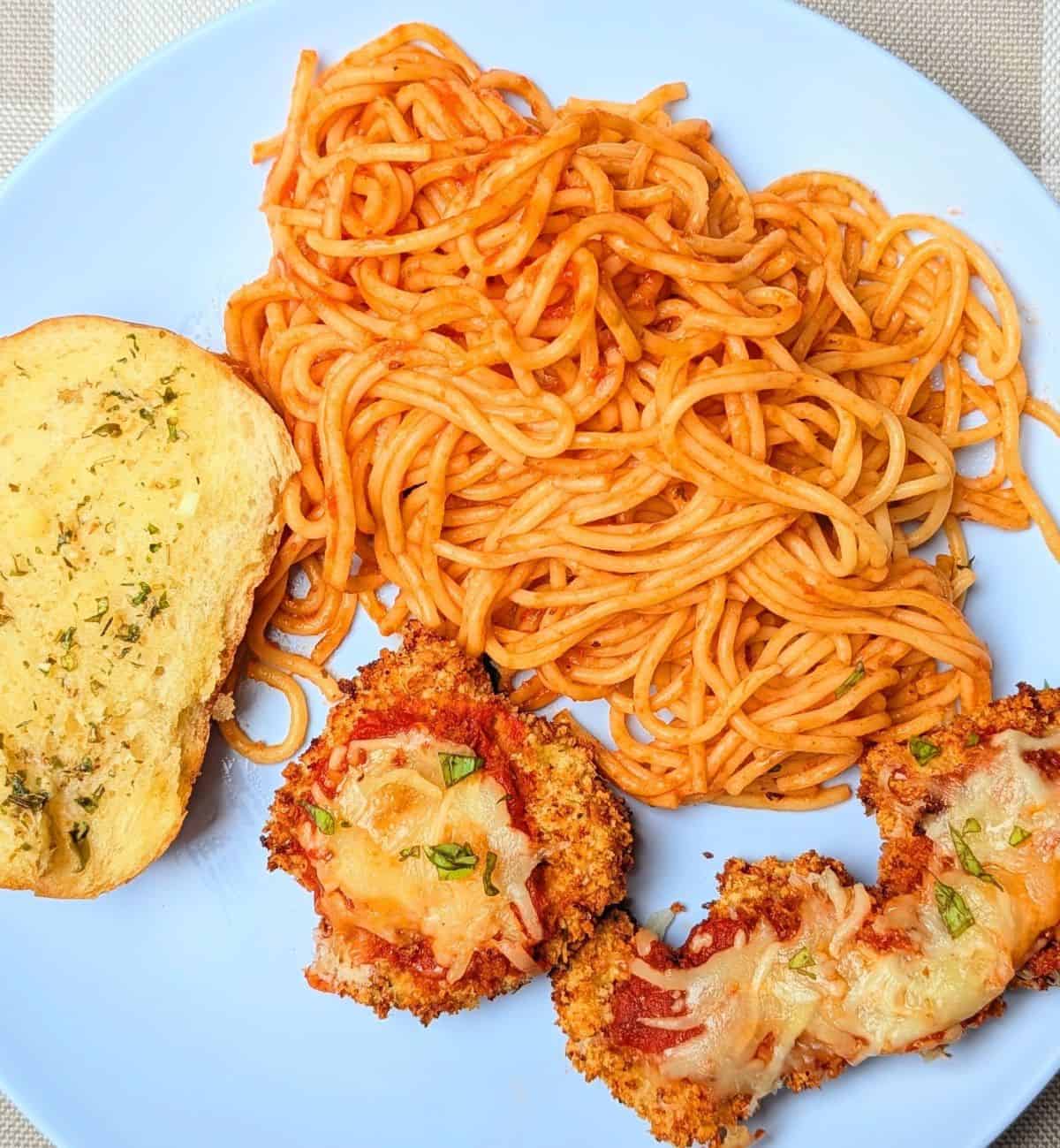 chicken parmesan cutlet on plate topped with mozzarella and basil, spaghetti, and bread