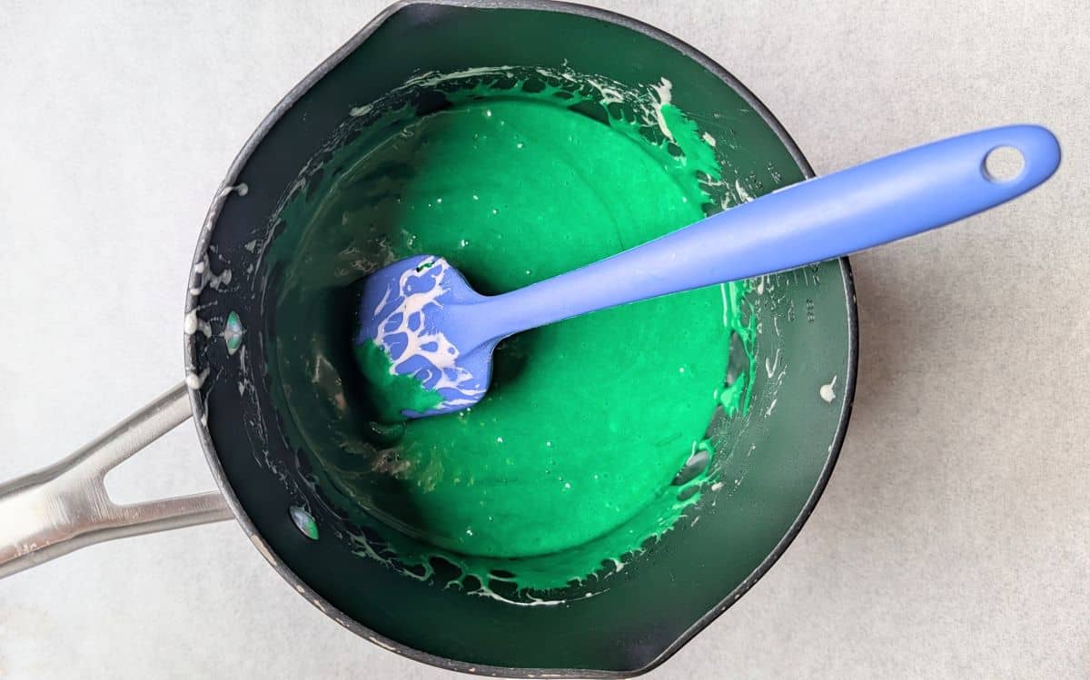 Adding green food dye and extracts to melted marshmallows in pan.