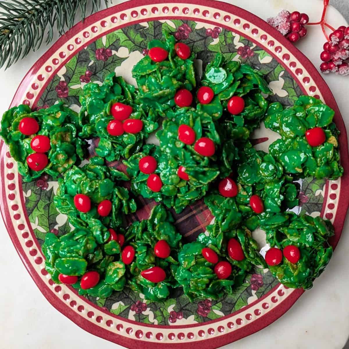 Homemade green holly cookies with red cinnamon candies served on a festive holiday plate.