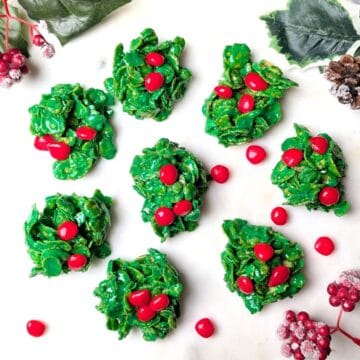 A serving tray of homemade green holly cookies topped with three red cinnamon candies for the holidays.