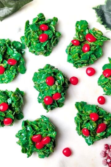 A serving tray of homemade green holly cookies topped with three red cinnamon candies for the holidays.