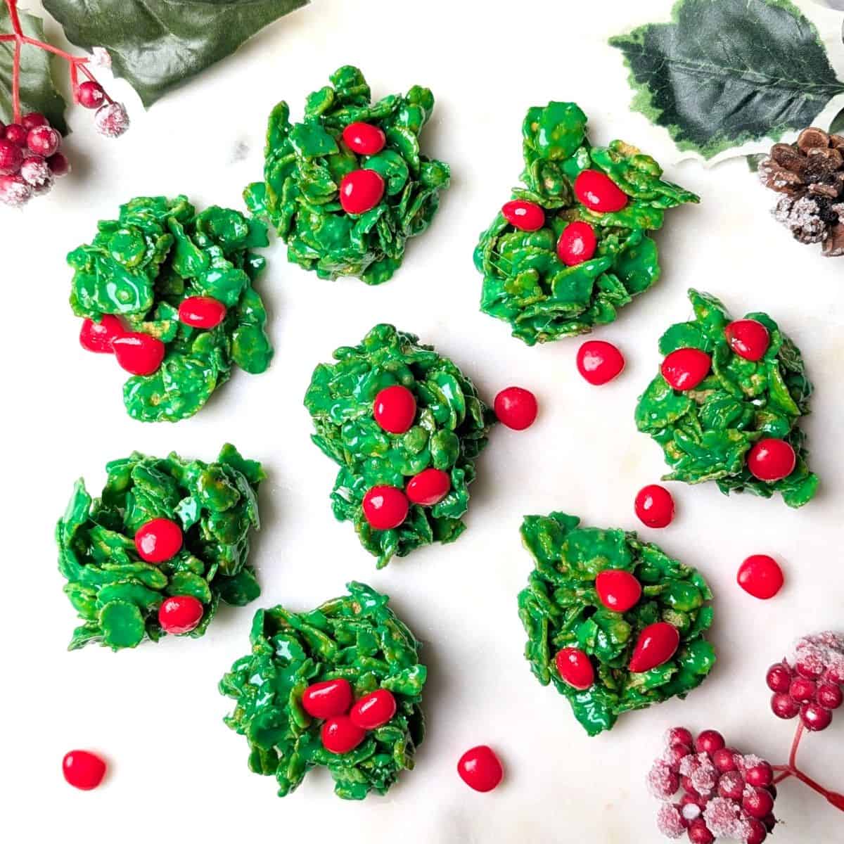 A serving tray of homemade green holly cookies topped with three red cinnamon candies for the holidays.