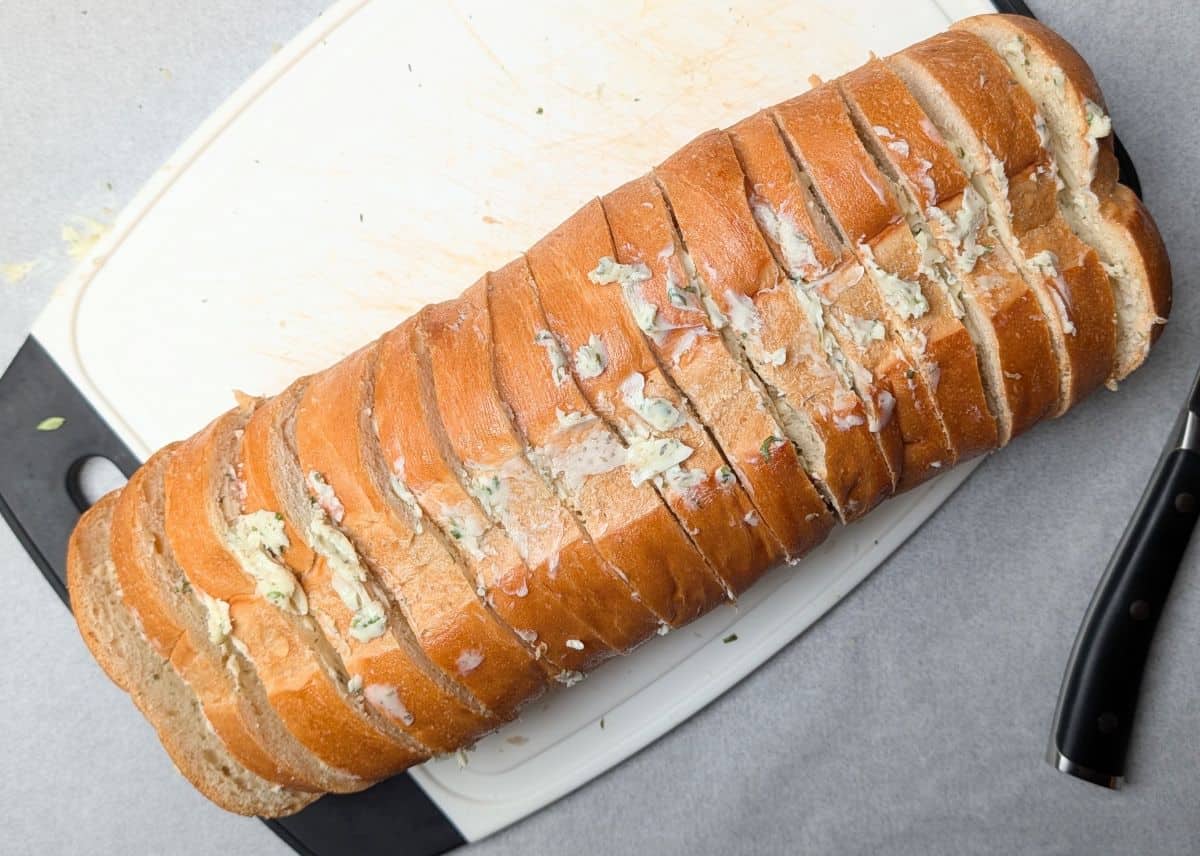 A sliced loaf of Italian bread generously spread with herb butter to make simple garlic bread.