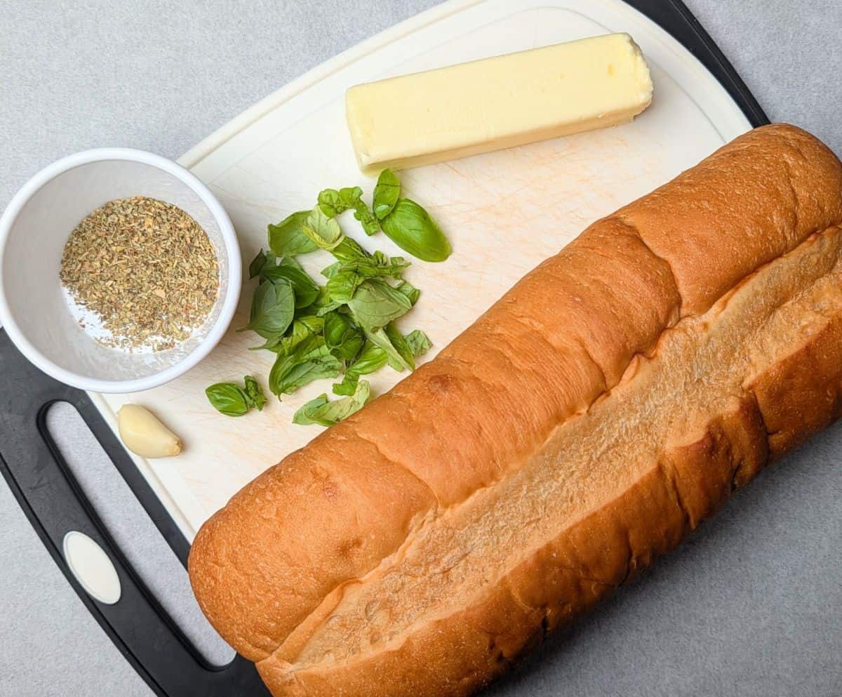 The fresh ingredients needed to make simple garlic bread, including a loaf of bread, butter, and fresh herbs.