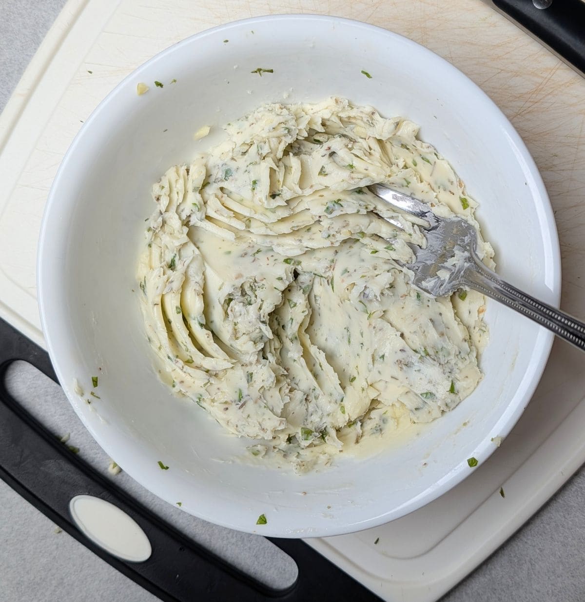 Mashing butter and fresh herbs with a fork to make a spread for simple garlic bread.