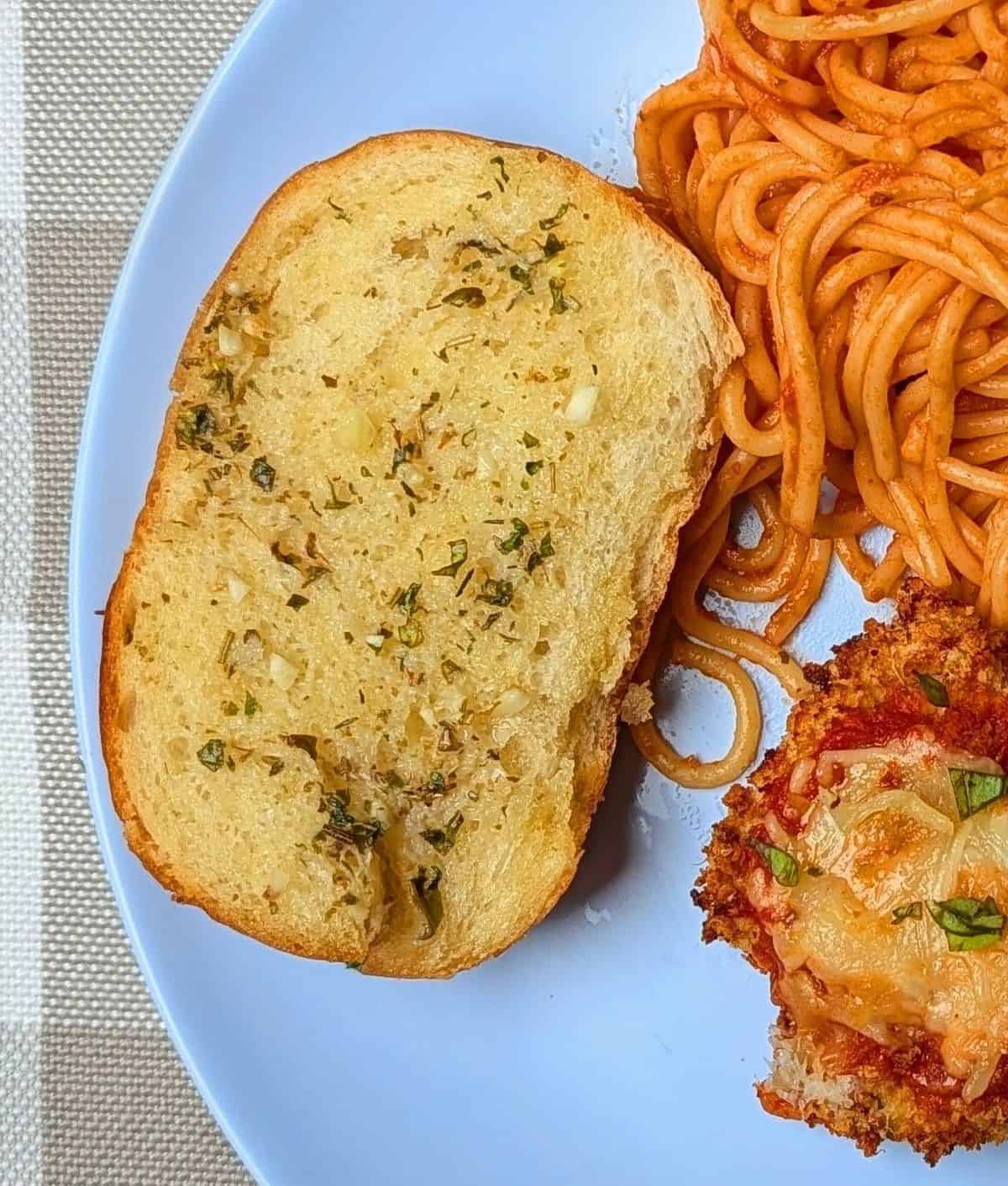 Close up of a warm piece of simple garlic bread paired with pasta.