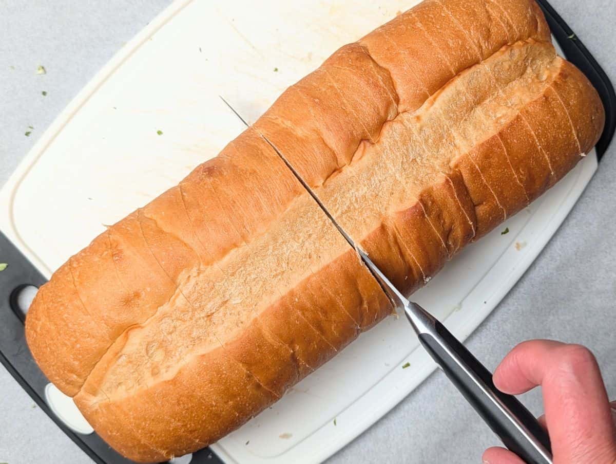 Slicing a loaf of Italian bread on a wooden cutting board with a bread knife.