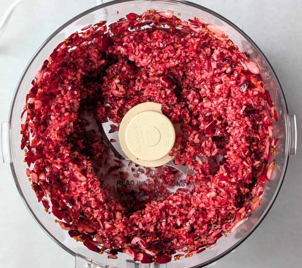 Overhead view of chopped fresh cranberries inside a food processor bowl for a cranberry fluff salad recipe.