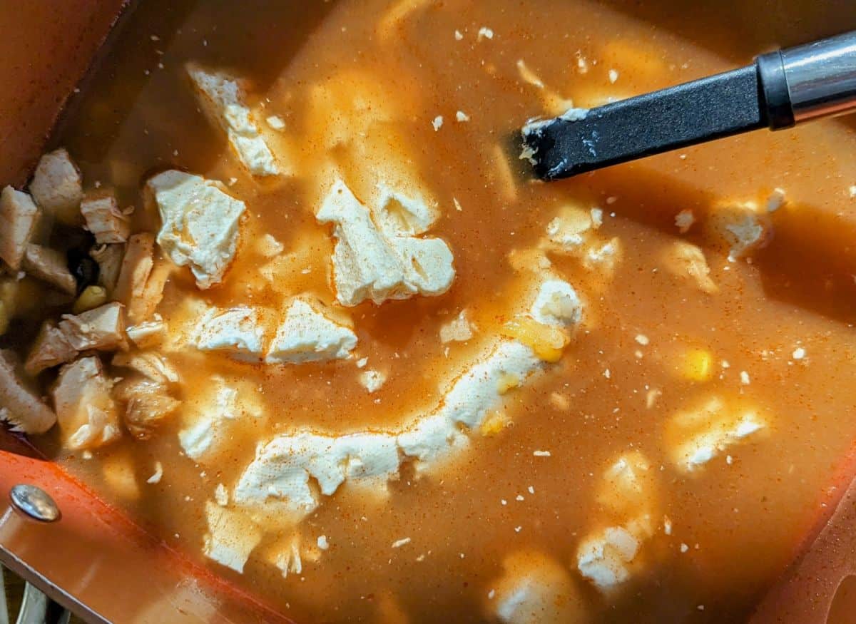 cold cream cheese being stirred into hot soup, creating flecks