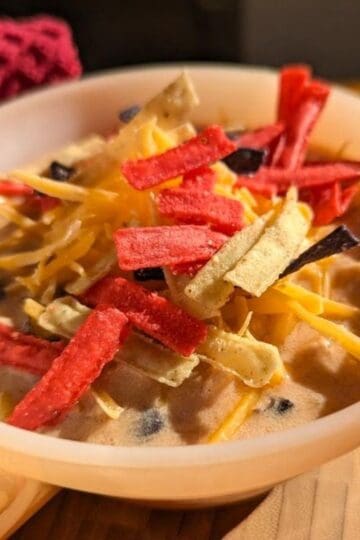 A bowl of creamy chicken enchilada soup topped with crispy tortilla strips, melted cheese, and green onions.
