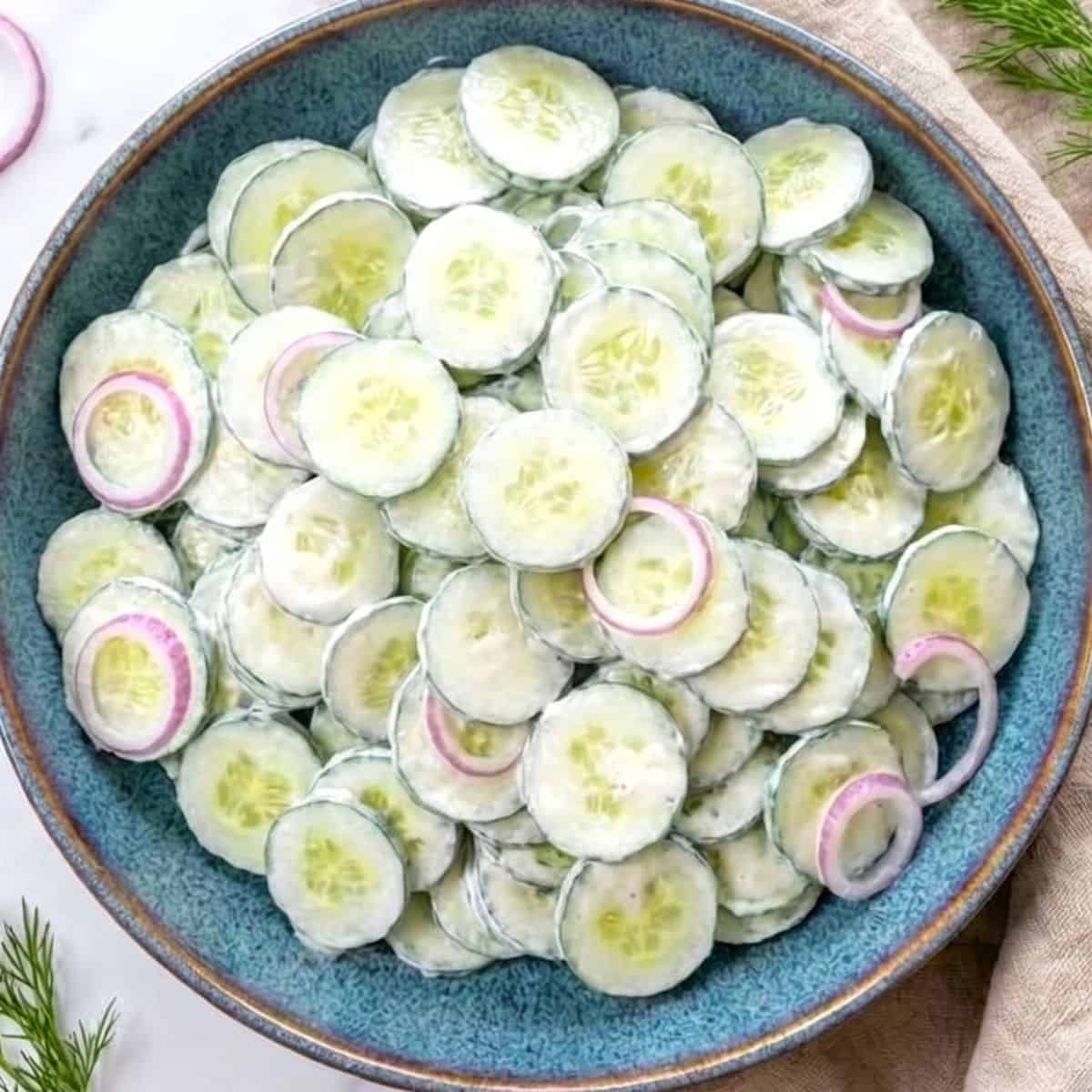 Creamy cucumber sour cream salad with fresh dill and red onions in a serving bowl.