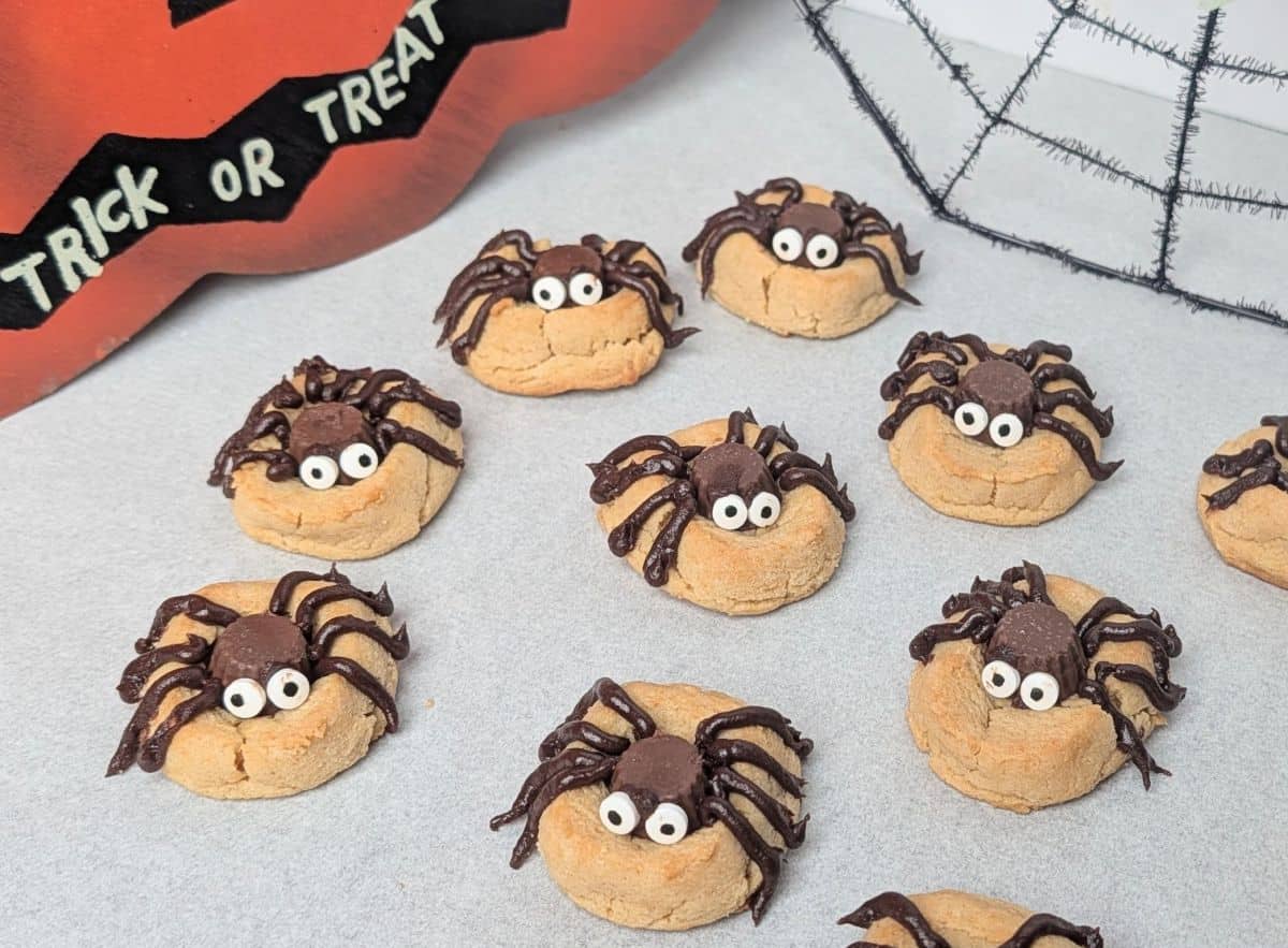 A white serving tray filled with homemade peanut butter Halloween spider cookies decorated with chocolate candy bodies, piped chocolate legs, and candy googly eyes.