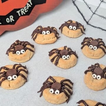 A white serving tray filled with homemade peanut butter Halloween spider cookies decorated with chocolate candy bodies, piped chocolate legs, and candy googly eyes.