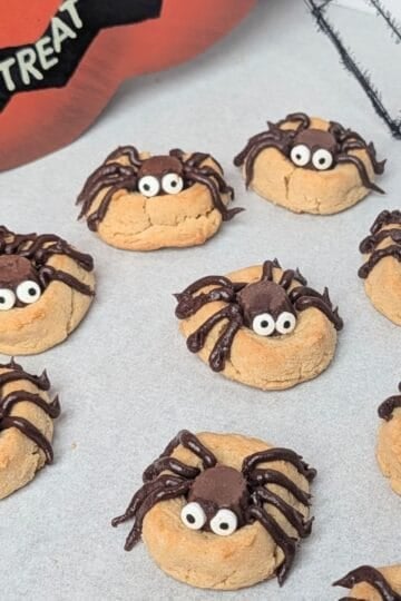 A white serving tray filled with homemade peanut butter Halloween spider cookies decorated with chocolate candy bodies, piped chocolate legs, and candy googly eyes.