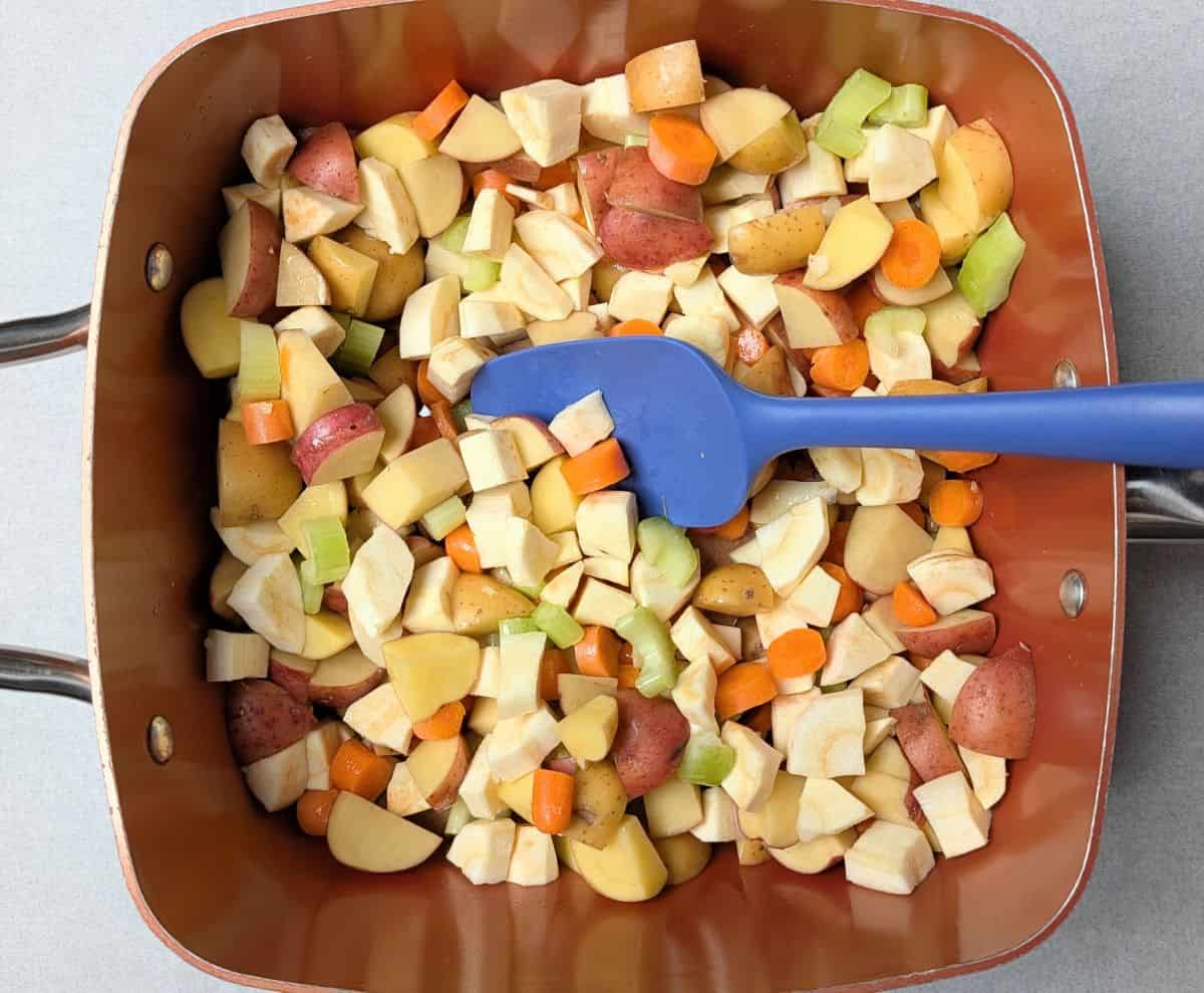 A blue spatula stirring fresh chopped vegetables, including carrots, potatoes, and onions, in a pot to make the filling for a healthy chicken pot pie.