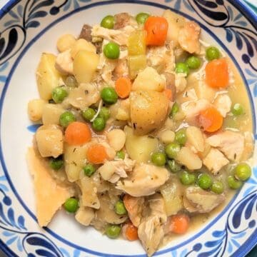 A serving of healthy chicken pot pie in a blue patterned bowl, showing tender chunks of chicken, peas, carrots, and potatoes, topped with pieces of golden baked pie crust.