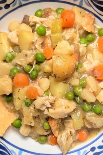 A serving of healthy chicken pot pie in a blue patterned bowl, showing tender chunks of chicken, peas, carrots, and potatoes, topped with pieces of golden baked pie crust.