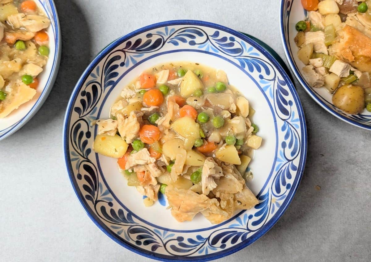 A single serving of healthy chicken pot pie in a bowl, featuring tender chicken, carrots, and peas topped with pieces of golden baked pie crust.