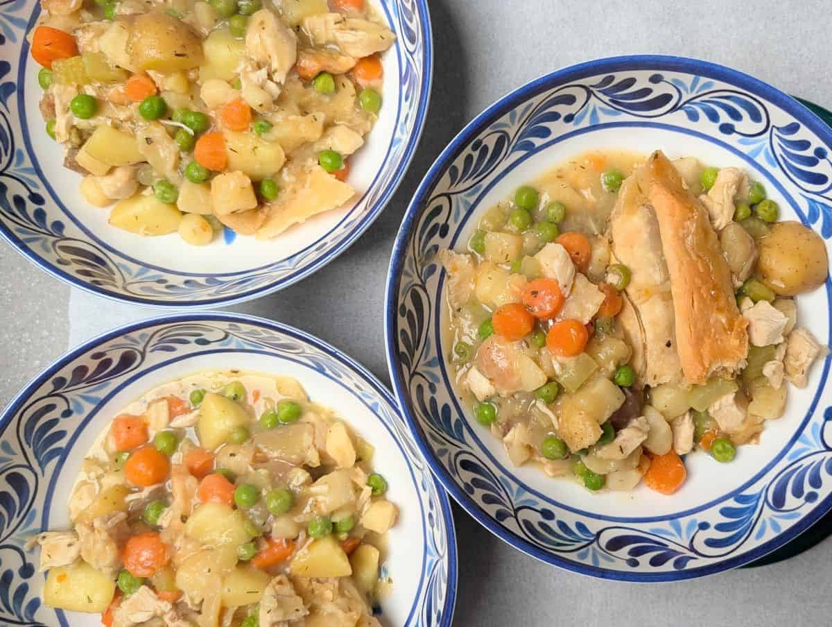 Three bowls filled with healthy chicken pot pie portions, showing pieces of crust, carrots, and peas ready to be served.